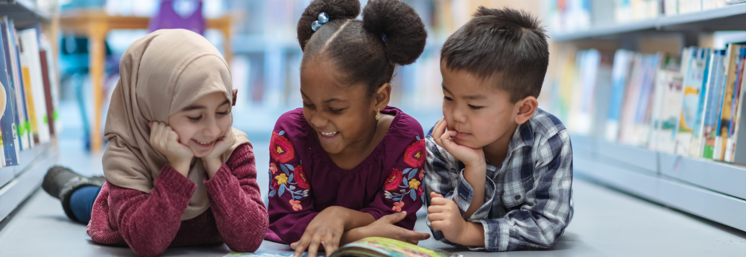 Photograph of 3 children reading a book together.