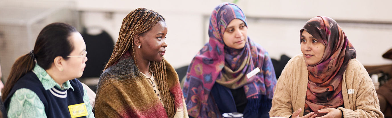 Photograph of 4 female partners / participants having a discussion around a table at the Flourishing Communities Learning and Celebration Event. Photograph by Photographer London: https://freelanceeventsphotographer.co.uk/